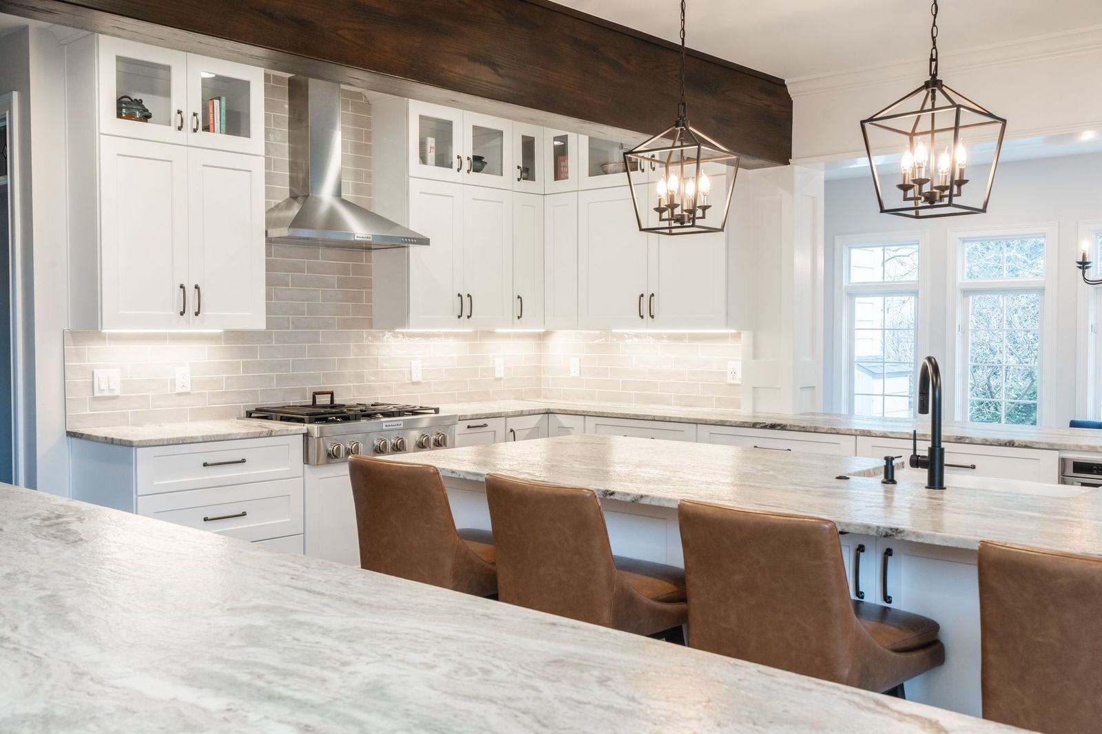 A kitchen with white cabinets , granite counter tops , and brown chairs.