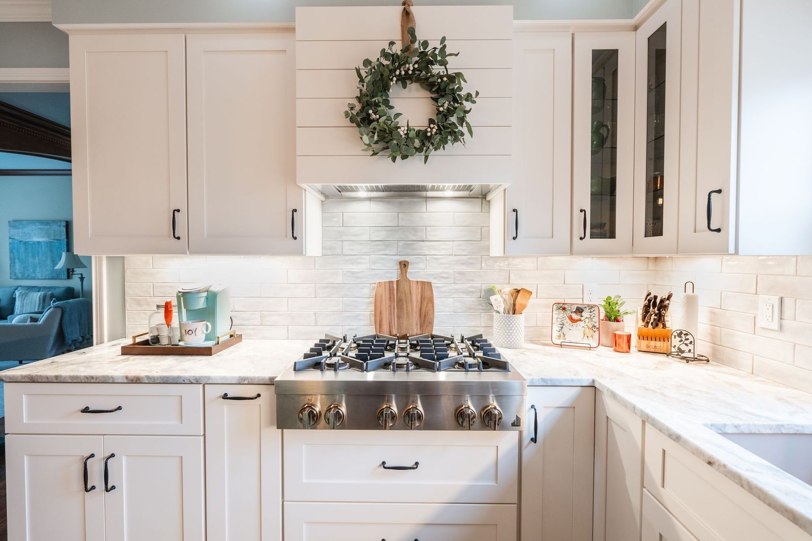 A kitchen with white cabinets and a stove top oven with a wreath hanging above it.