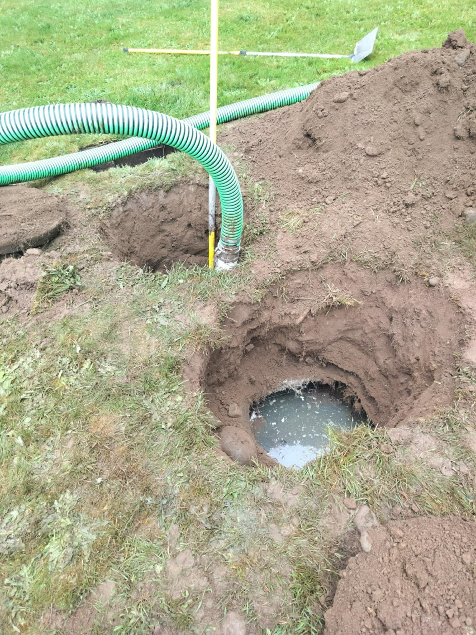 Holes dug in a grassy area with water and a green hose, possibly for well or septic system work.