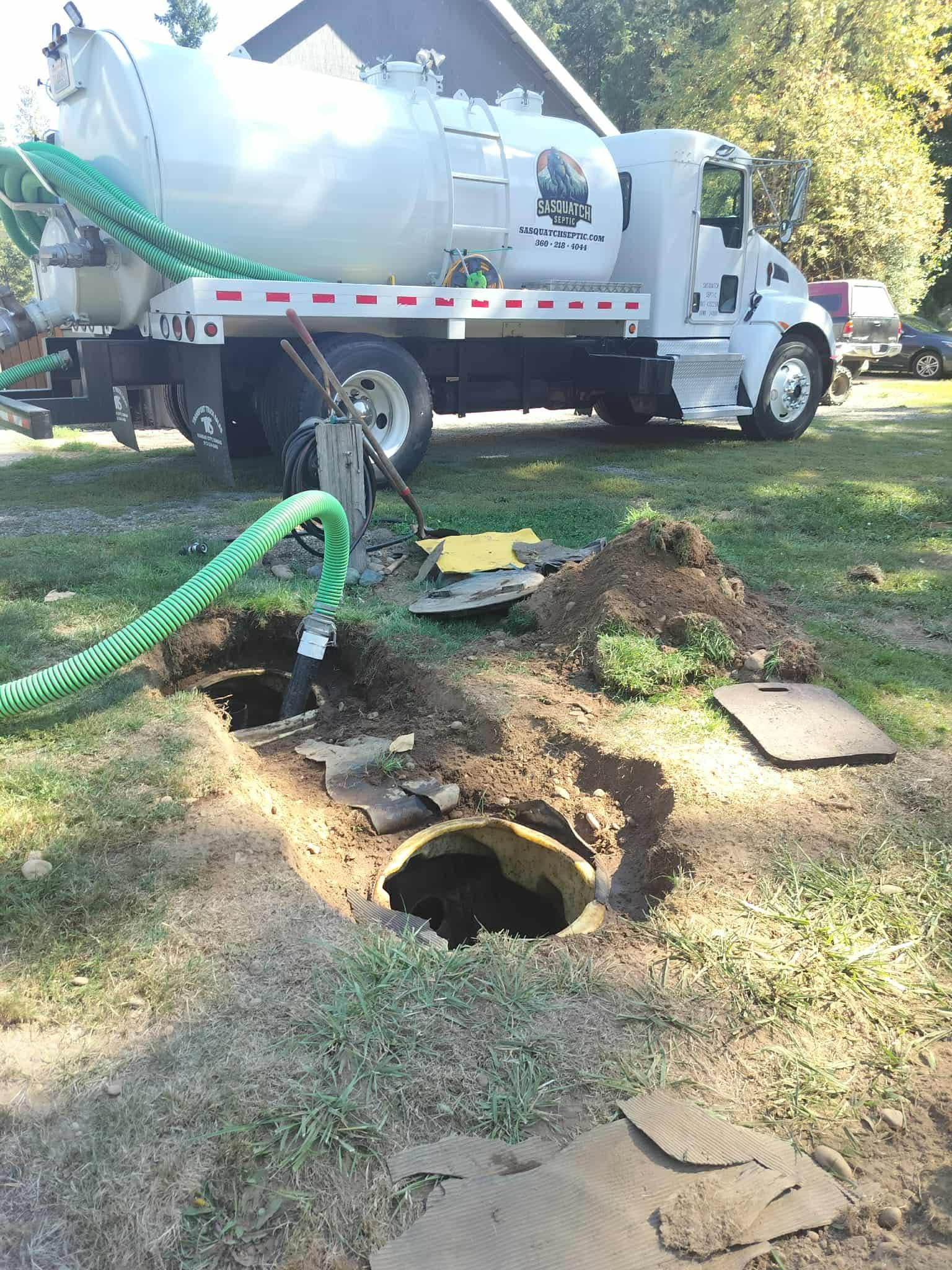 Septic tank being serviced by a white truck with a large tank; hoses connected to open underground tanks.