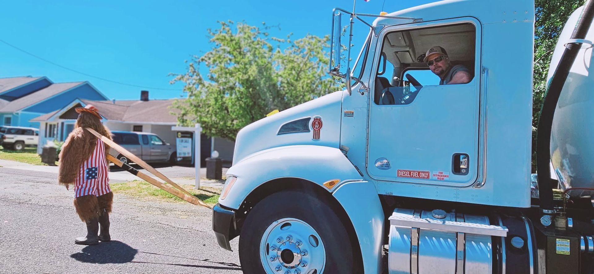 A person in a bear costume pulls a truck with a wooden plank on a sunny day.