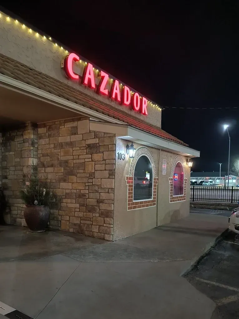 A nighttime view of a restaurant with a stone facade and a large, glowing red 