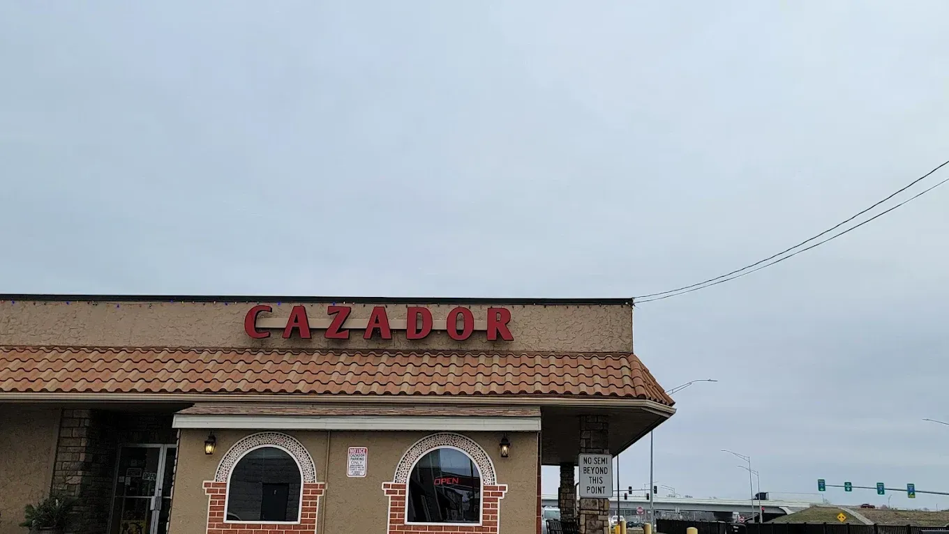 A Cazador Mexican restaurant building with a tan stucco exterior, red signage, and arched windows under a tile roof.
