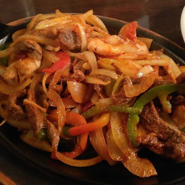 Stir-fried noodles with shrimp, beef, and colorful peppers in a dark bowl
