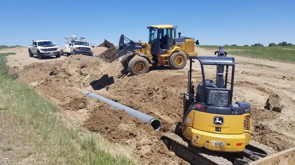 A group of construction vehicles are working on a dirt road.