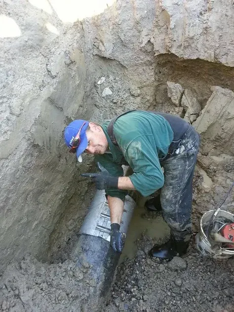 A man is working on a pipe in the dirt