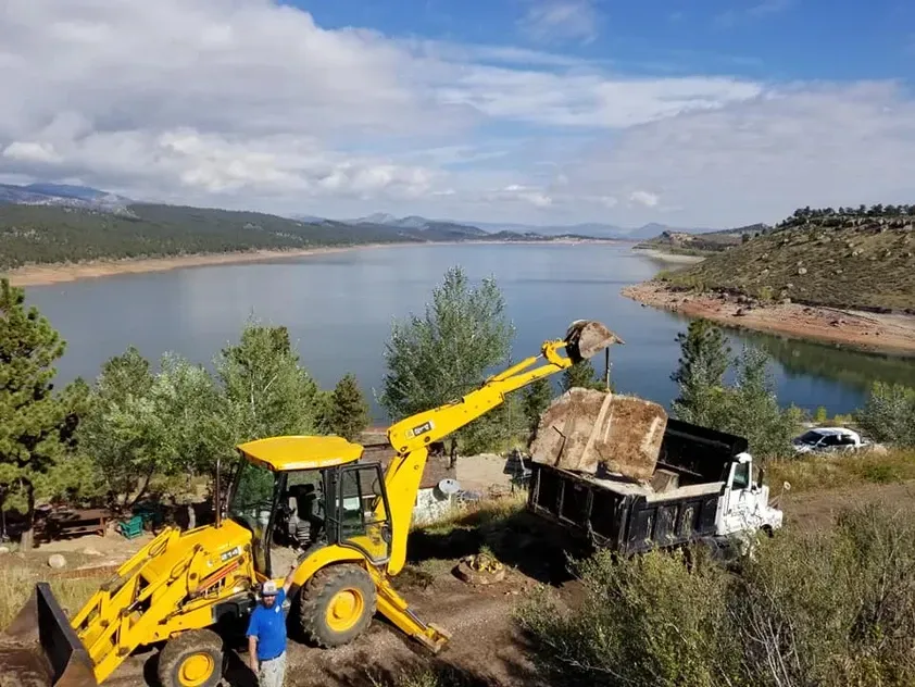 A man is standing next to a yellow bulldozer near a lake.