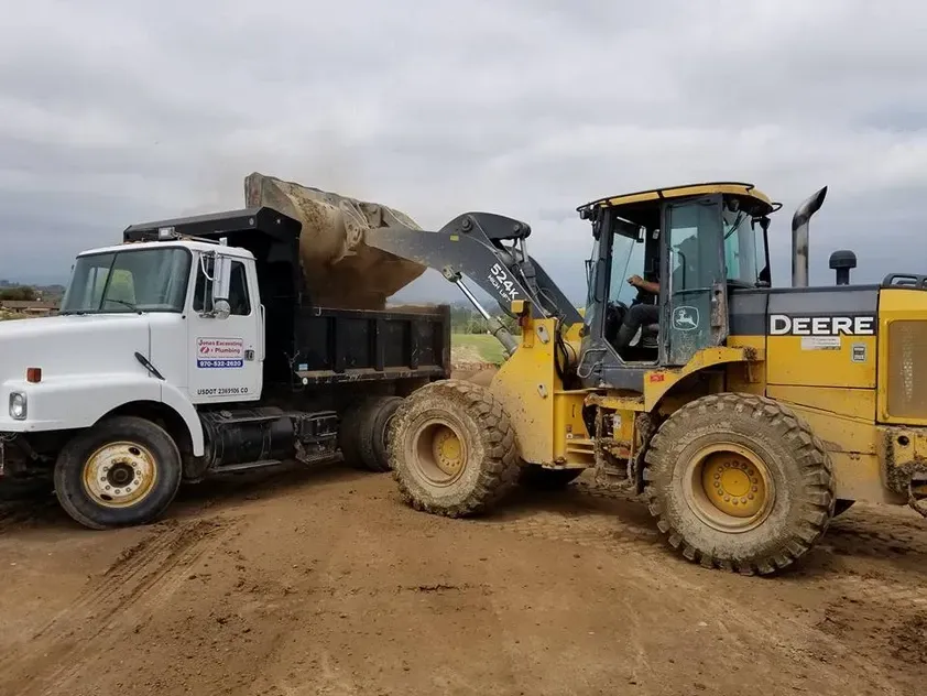 A dump truck is being loaded with dirt next to a deere wheel loader.