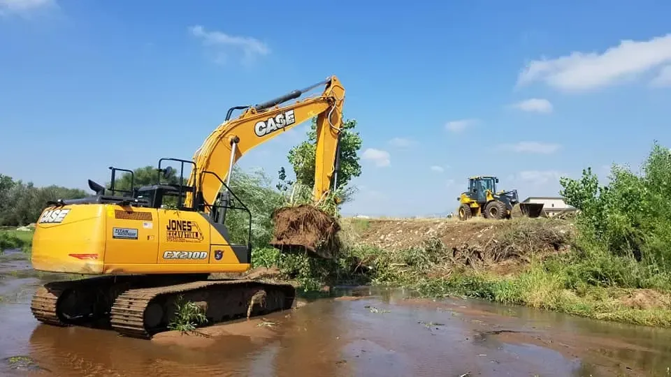 A yellow excavator is digging in a muddy river.