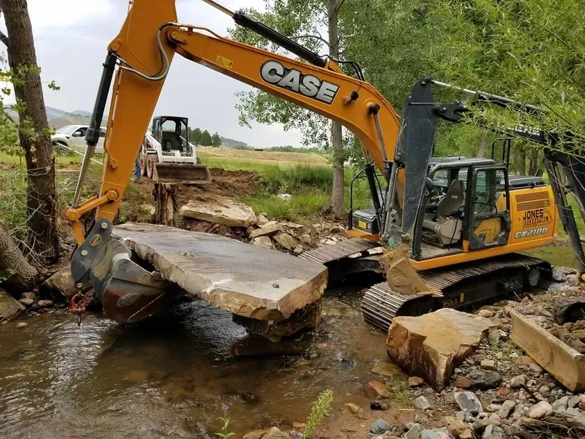 A case excavator is working on a bridge over a stream.