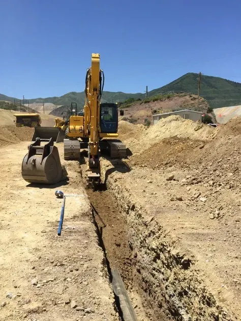 A yellow excavator is digging a trench in the dirt.