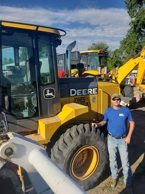 A man is standing in front of a yellow deere tractor.
