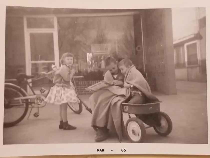 A black and white photo of three children playing with a wagon