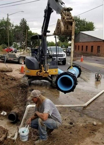 A man is kneeling in the dirt next to a large pipe
