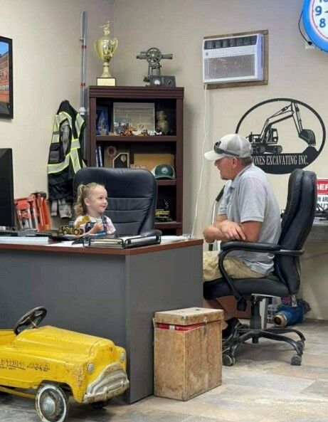 A man and a little girl are sitting at a desk in an office.