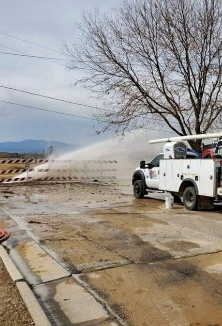 A white truck is spraying water from a hose on the side of the road.