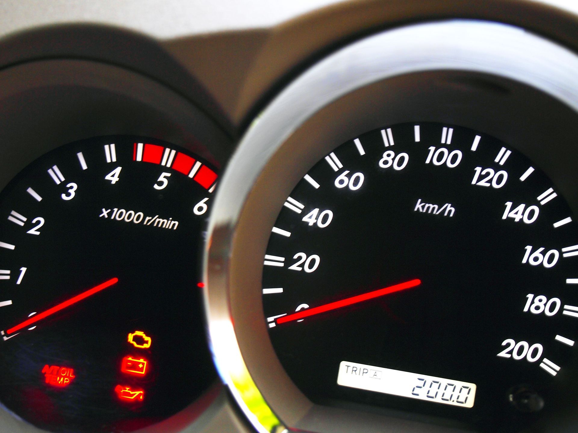 Car dashboard with gauges. Speedometer shows 80 km/h, tachometer at 5000 rpm. Warning lights are on.