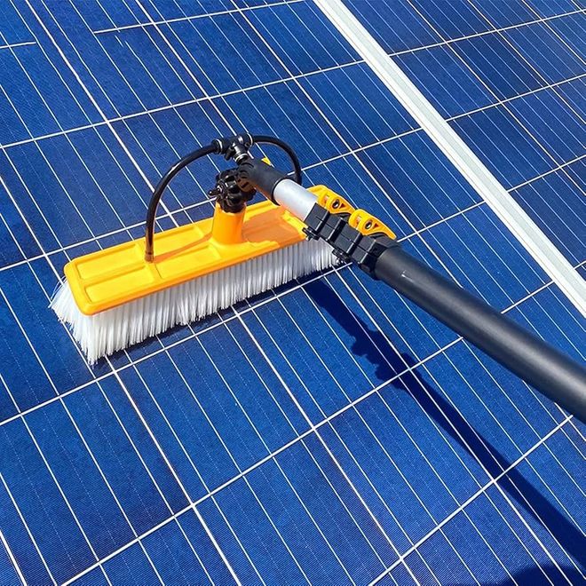 Solar panels being cleaned with a long-handled brush, with water streaks on the surface.