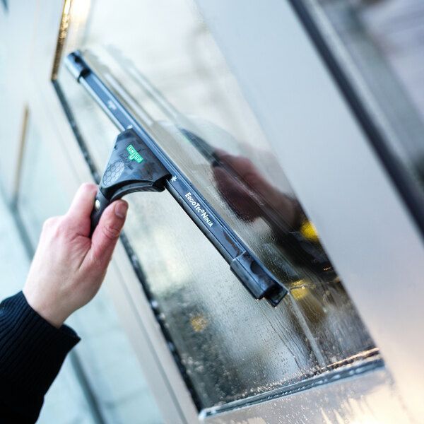 Purple-gloved hands cleaning window blinds with an orange sponge