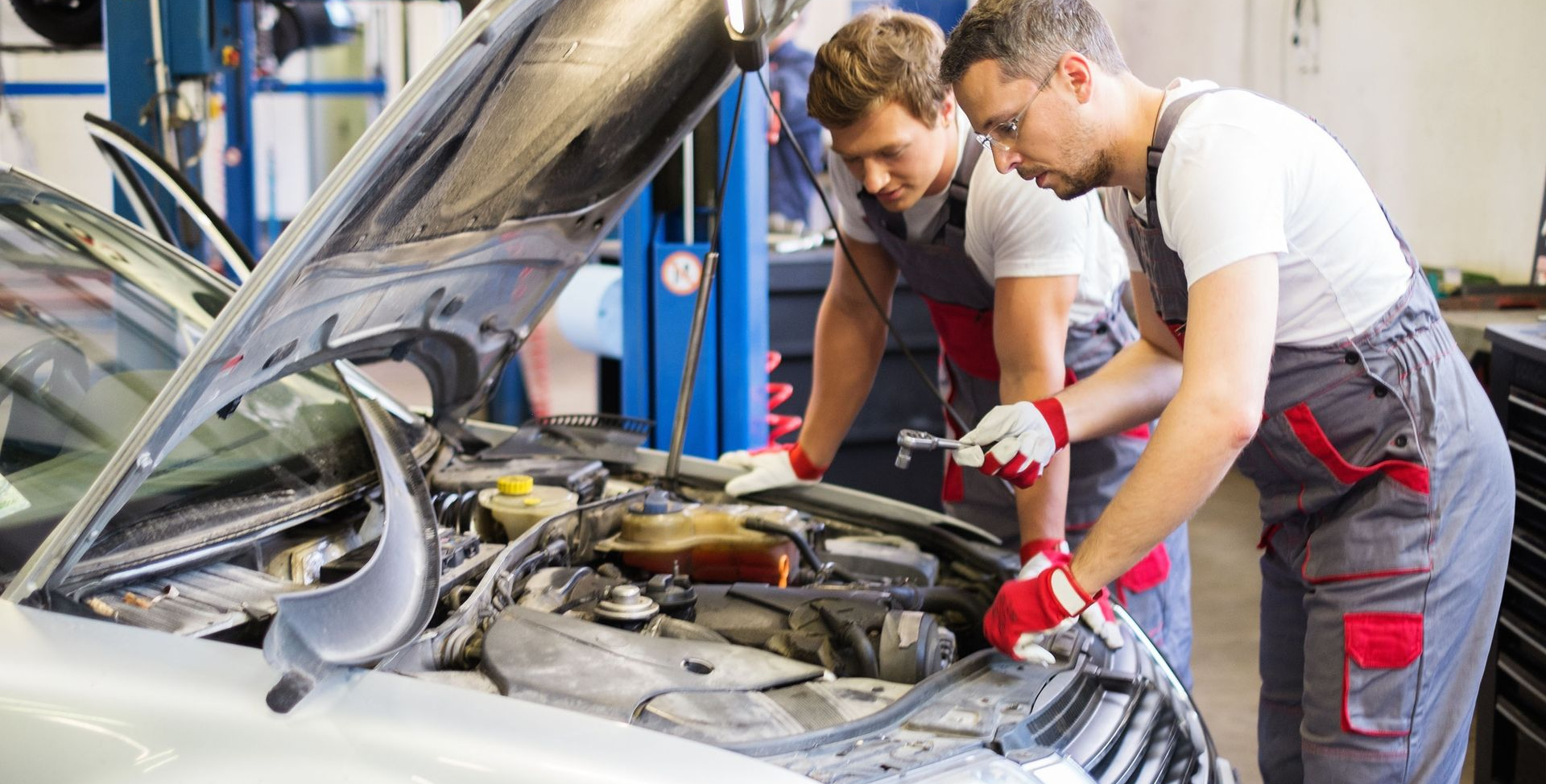 Two mechanics in coveralls working on a car engine in a garage.