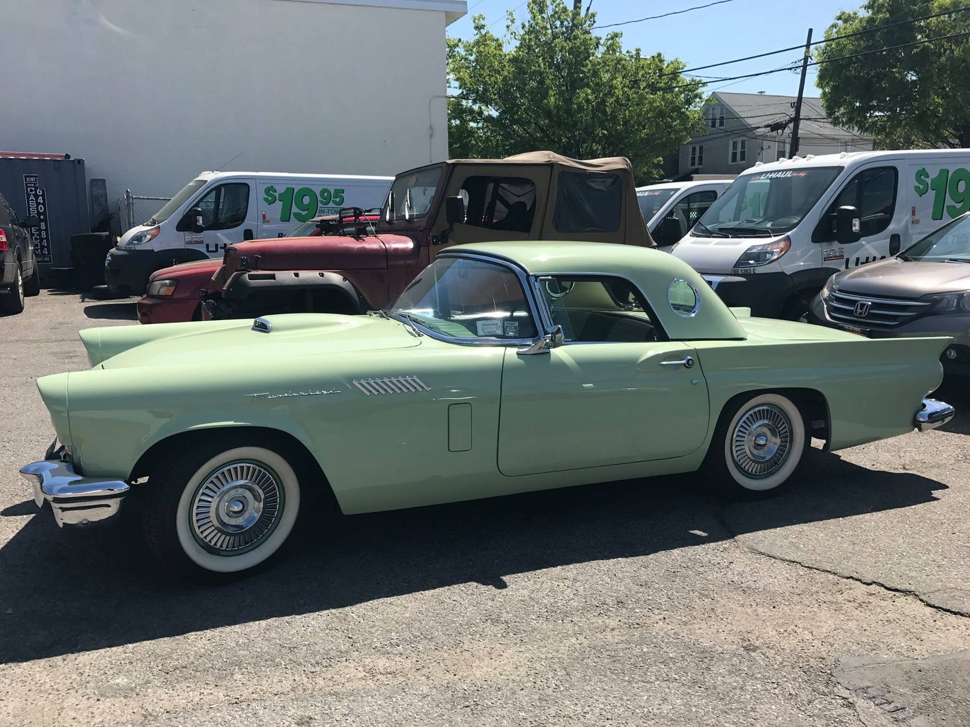 Green vintage Ford Thunderbird parked outside, next to other vehicles.