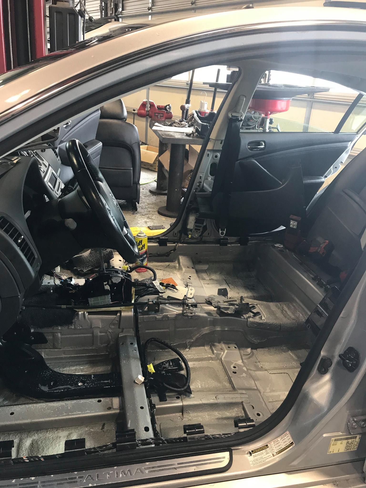 Car interior stripped down, revealing metal floor, dashboard, and seat frame, in a repair shop.