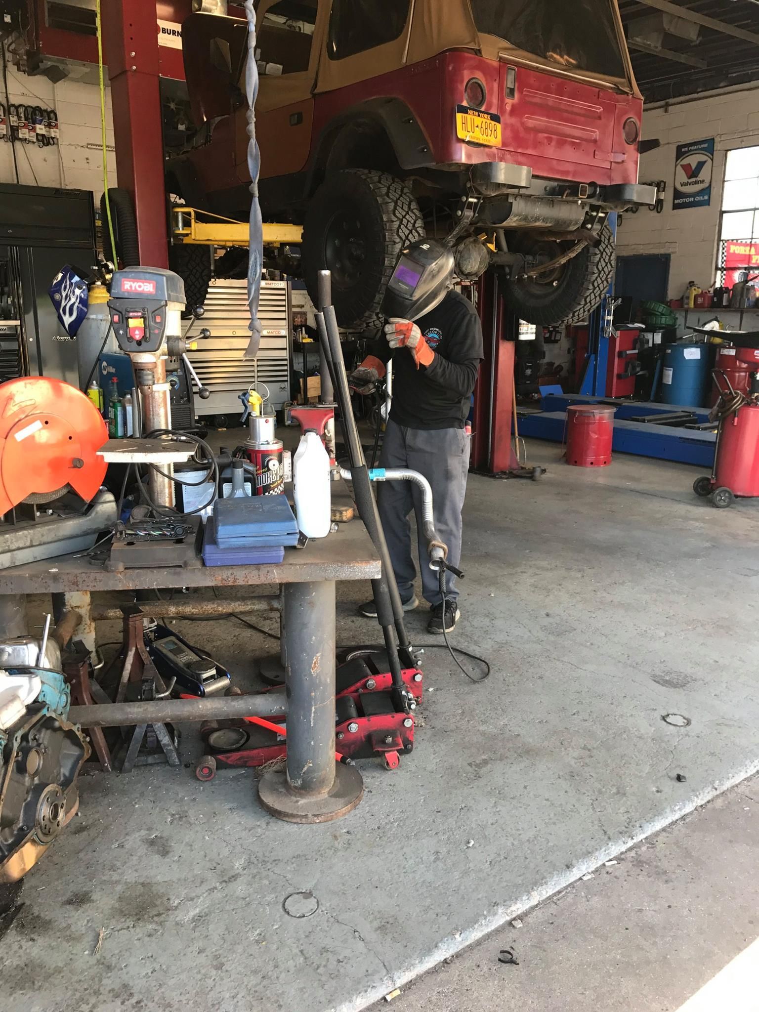 A mechanic welds under a lifted Jeep in a garage.