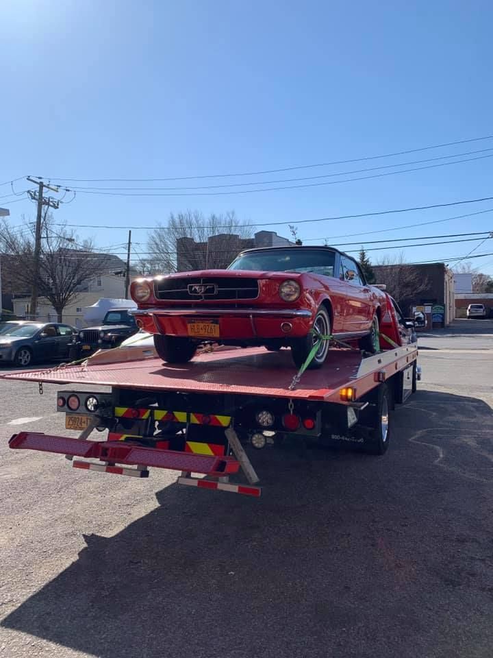 Red vintage convertible car on a flatbed tow truck on a sunny day.