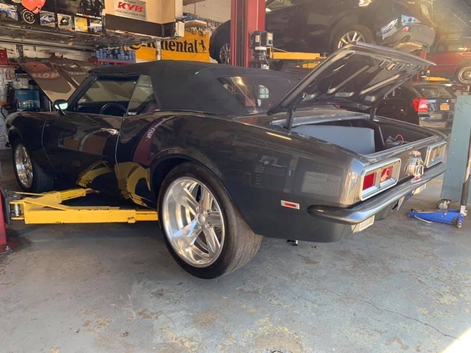 Dark grey classic convertible car in a garage with hood and trunk open, on a lift.