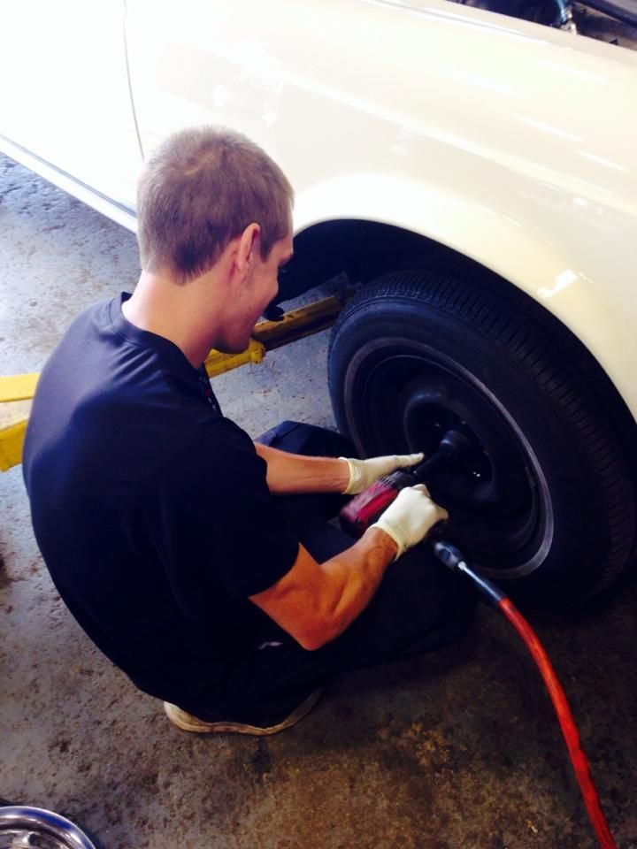 A person using a pneumatic wrench to remove a tire from a white car in a garage.