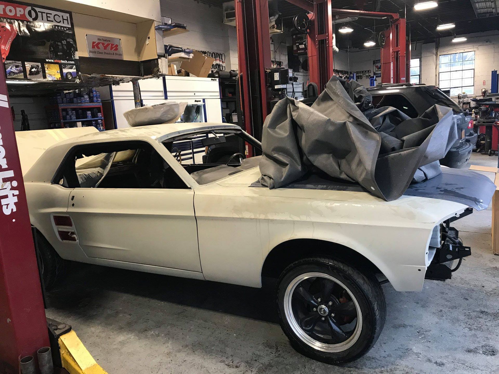 Classic white muscle car in a workshop, partially covered, undergoing restoration.