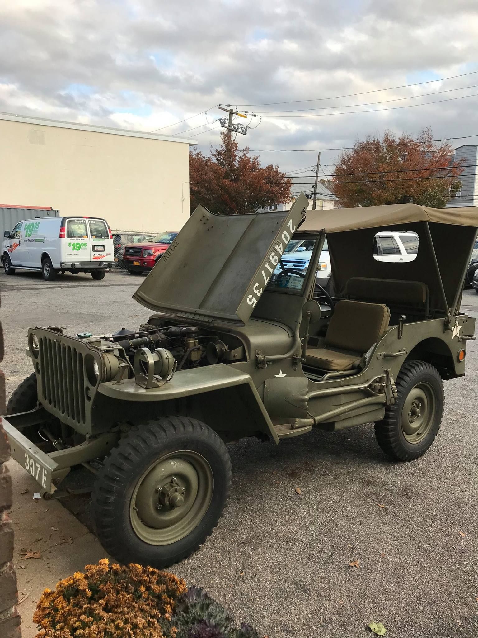 Olive green Jeep with hood up, canvas top, parked outdoors.