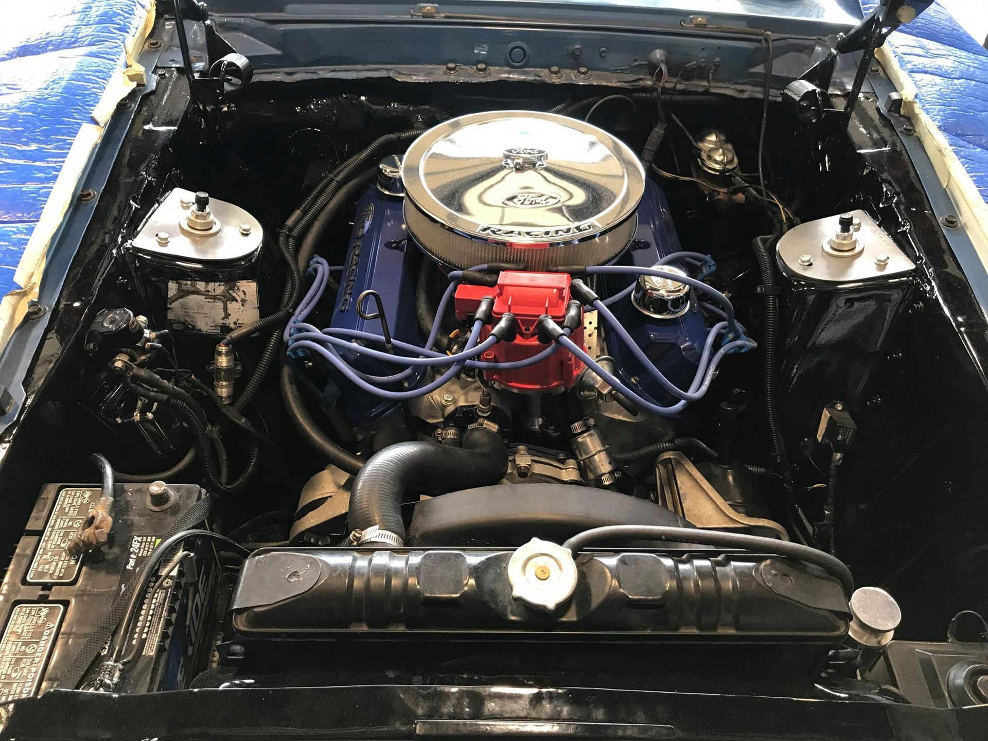 Blue engine in a classic car, with a chrome air filter, red distributor cap, and black engine bay.