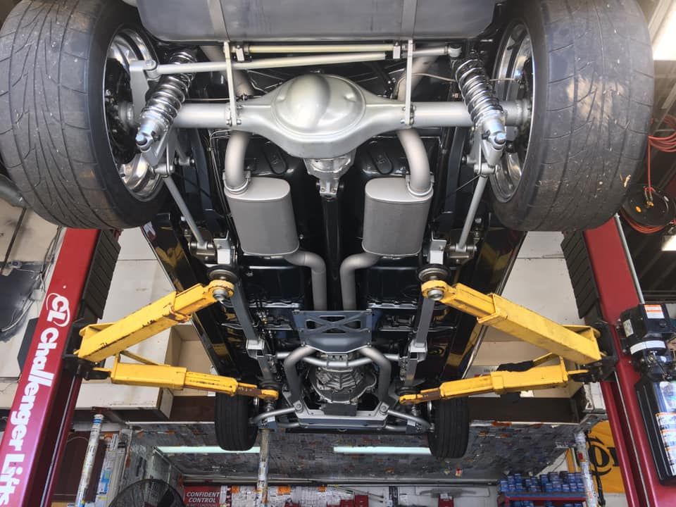 Undercarriage of a classic car on a lift, showing exhaust system, suspension, and large tires.