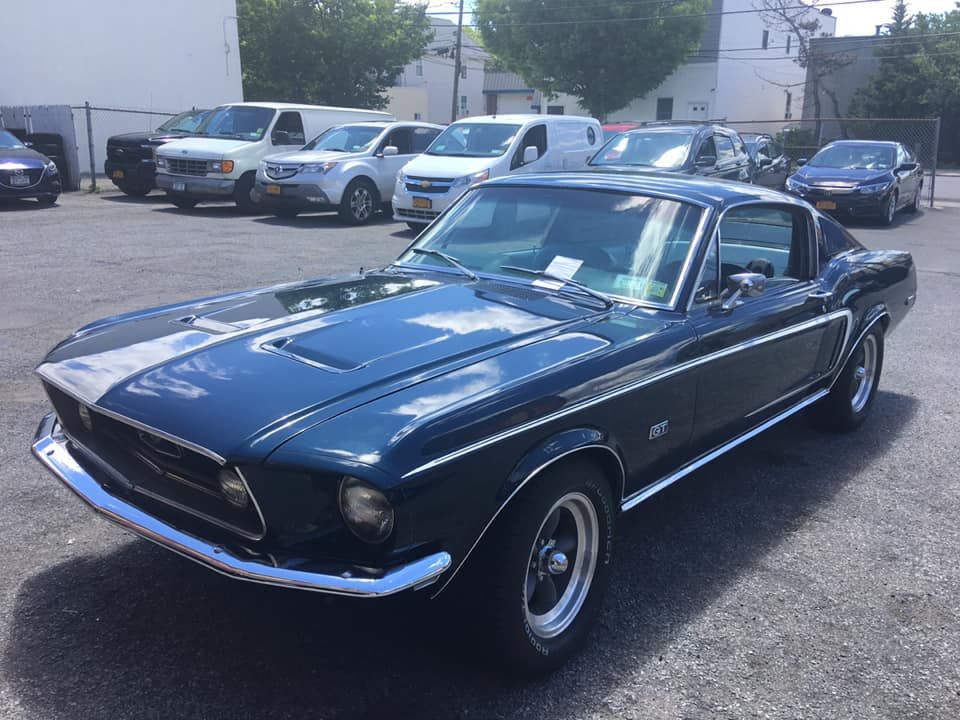 Dark blue 1968 Ford Mustang fastback with white racing stripes parked outside in a sunny parking lot.