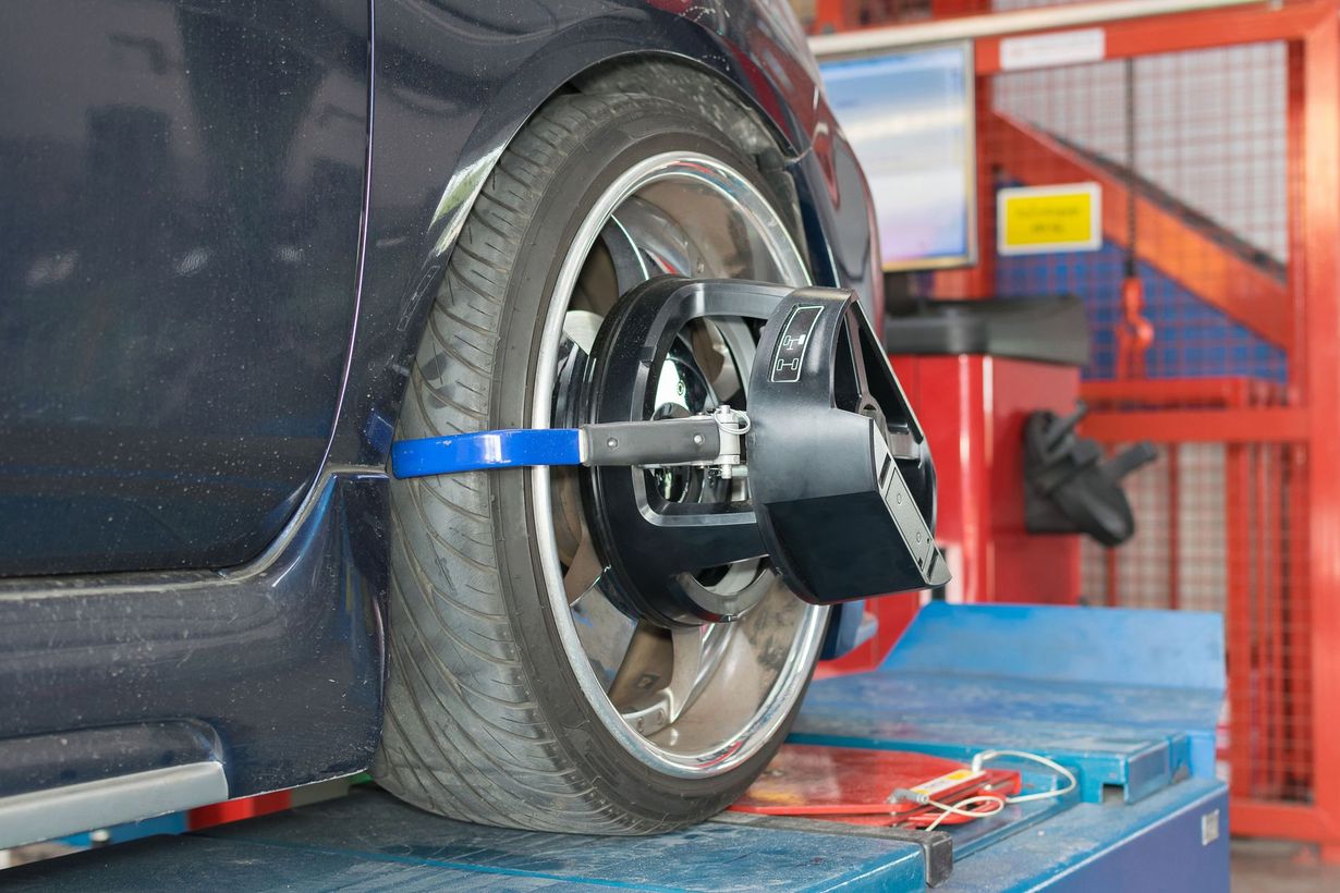 A car tire being aligned at an auto repair shop with a black alignment tool attached to the wheel.