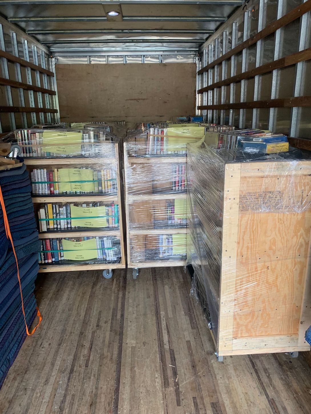 Inside a cargo truck, stacked pallets and boxes are wrapped in plastic along the aisle.