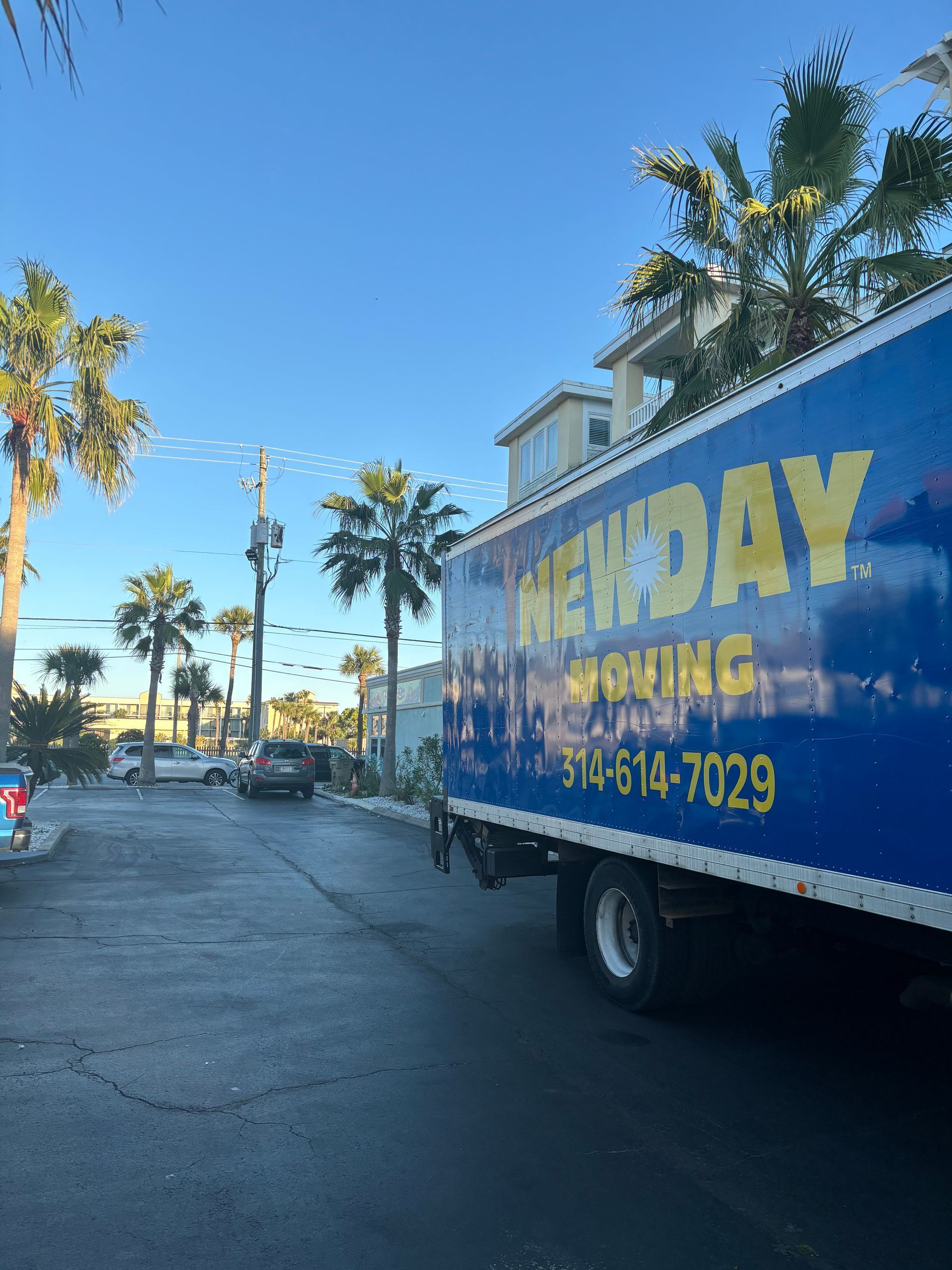 Blue moving truck with yellow lettering parked on a sunny palm-lined street