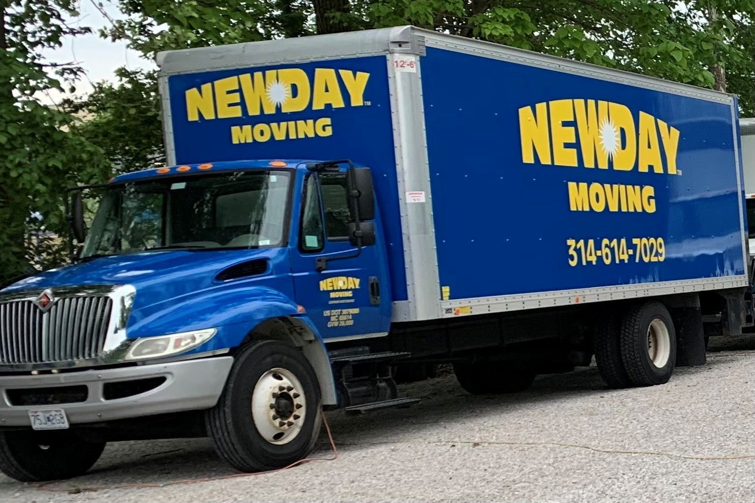 Blue Newday Moving box truck parked outdoors on gravel, with yellow company logo and phone number.