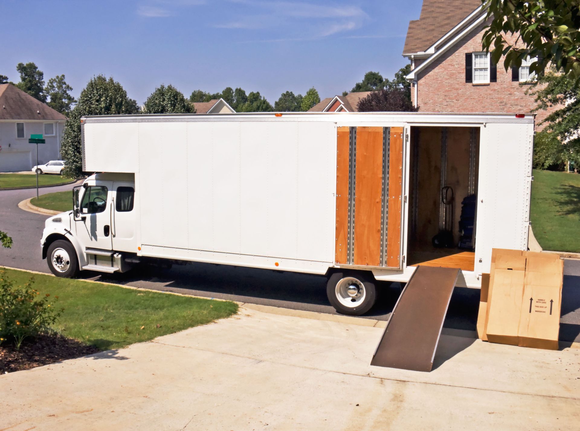 Moving truck parked in a driveway; ramp extended. A cardboard box sits nearby.