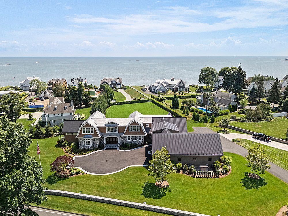 Large house with waterfront view, blue sky, and green lawn.