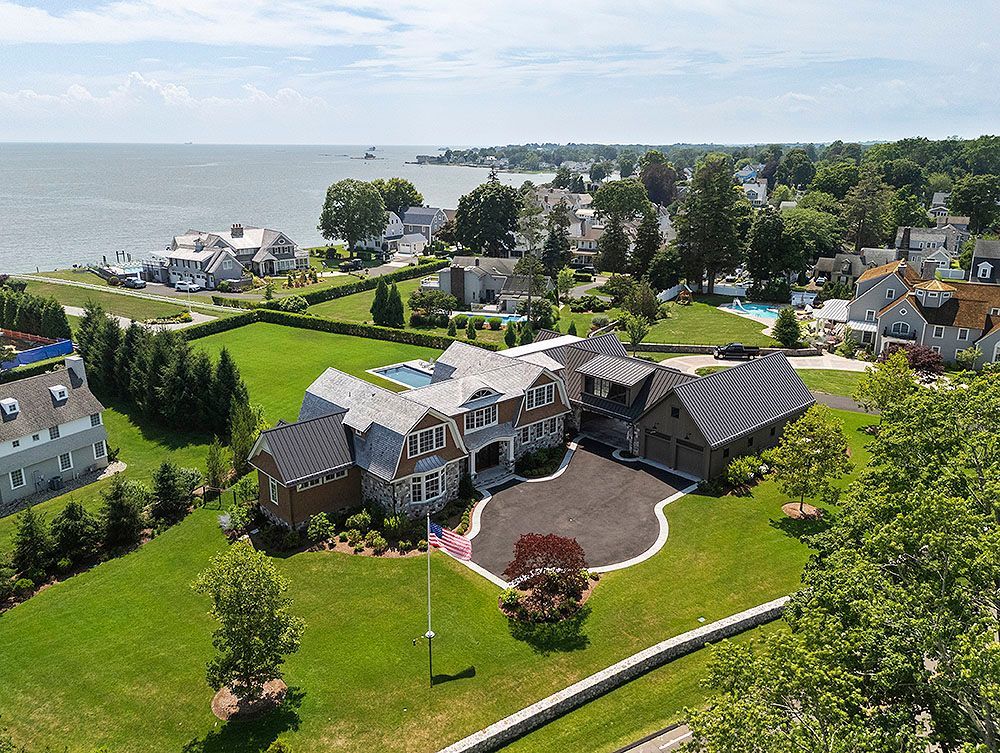 Aerial view of a large house with a dark driveway on a green lawn by the sea.