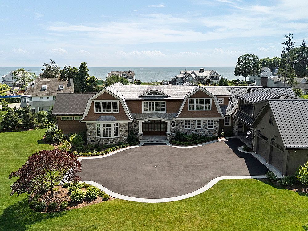 Luxurious house with a curved driveway on a green lawn, ocean view, blue sky.