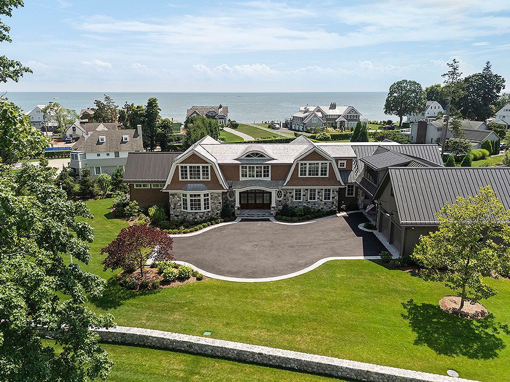A large, luxurious house with a circular driveway and view of the ocean.
