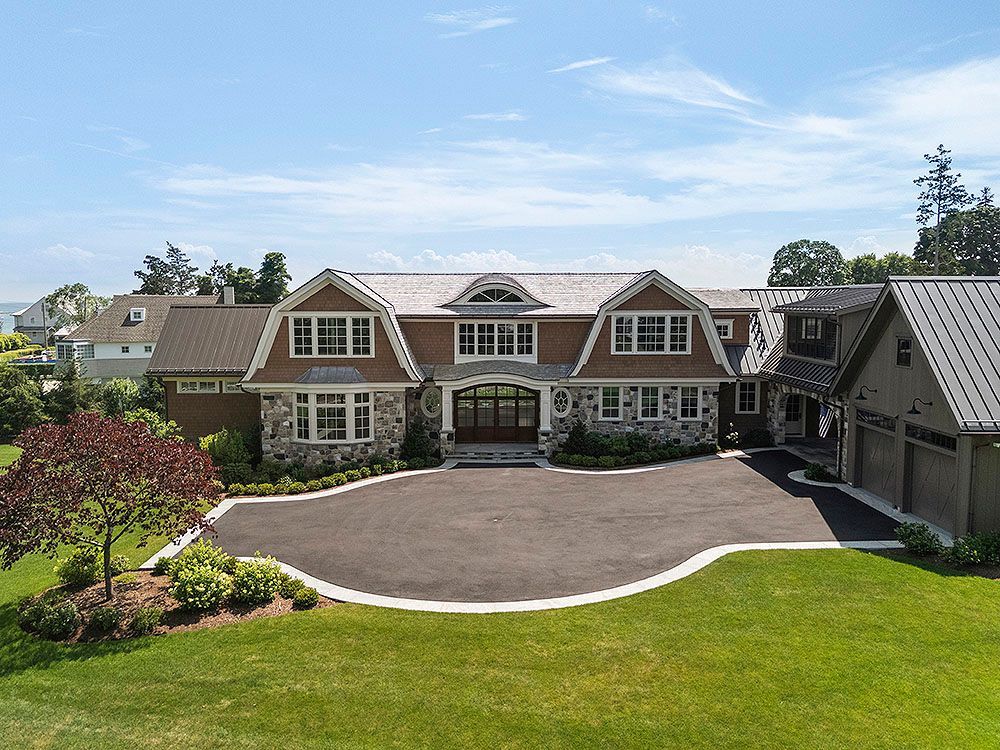 Large stone and wood house with a circular driveway on a grassy lawn.