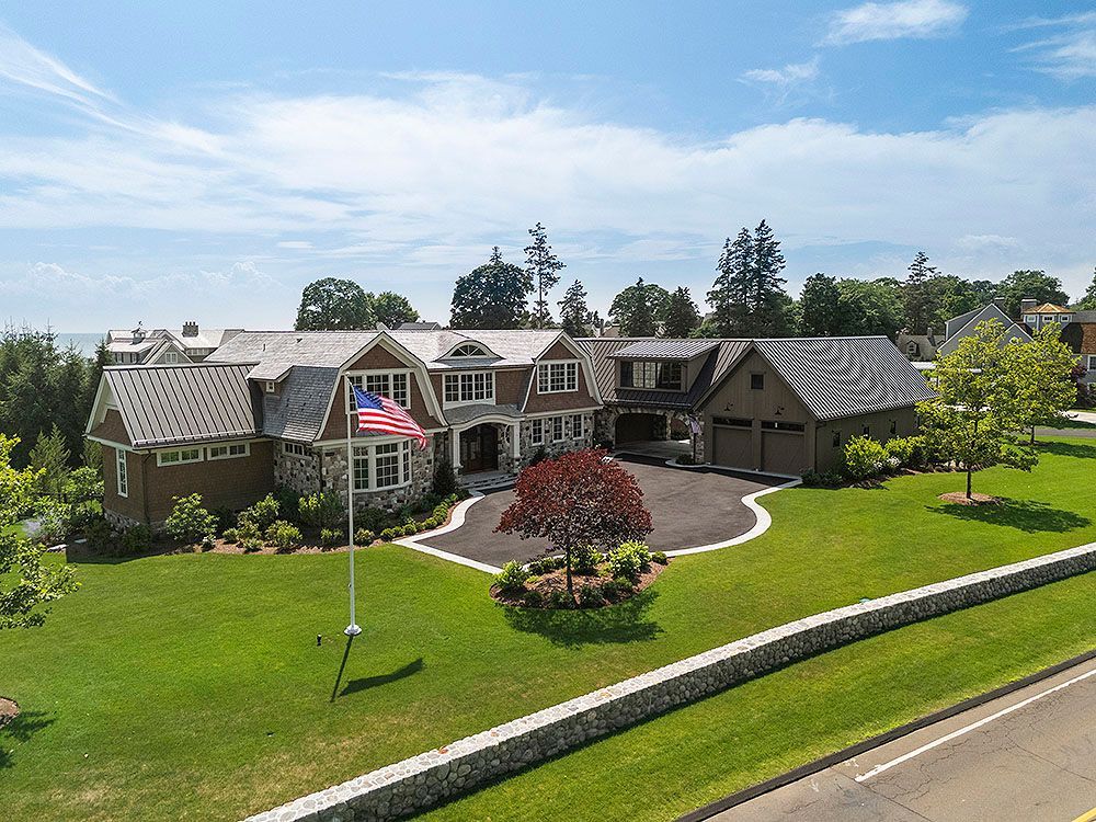 Large, multi-story brown house with an American flag on a green lawn.