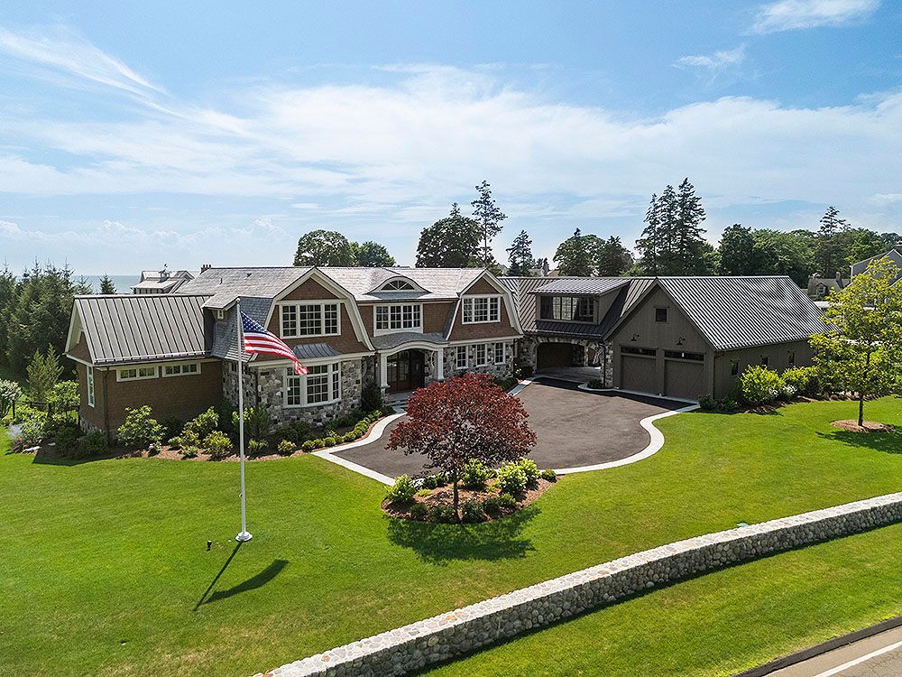Large brown and stone house with American flag on a green lawn.