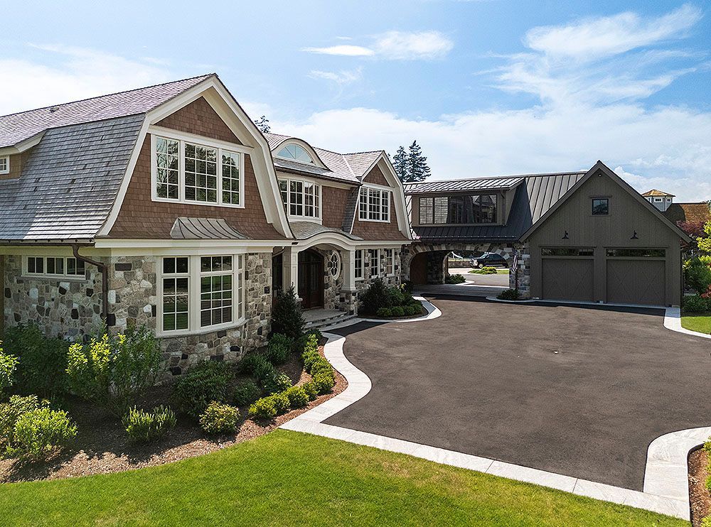 Large, luxurious home with stone and wood exterior, attached garage, and curved driveway on a sunny day.