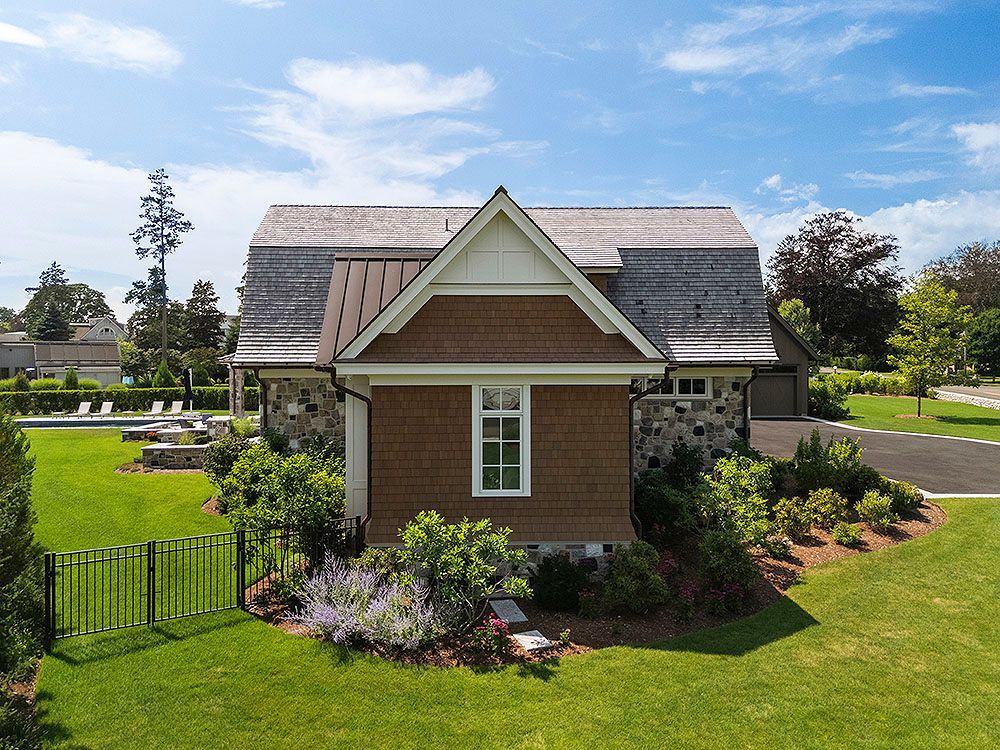 Small, brown-sided building with a wooden shingled roof on a grassy property with a pool and trees.