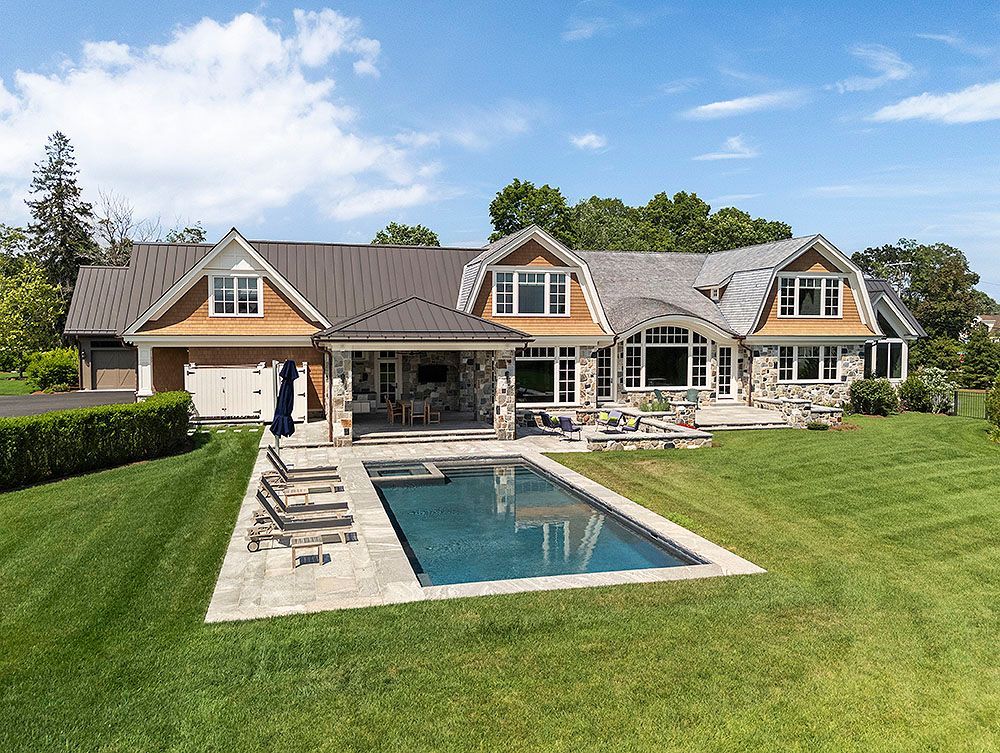 A large, stone house with a pool in the backyard, surrounded by green grass under a blue sky.
